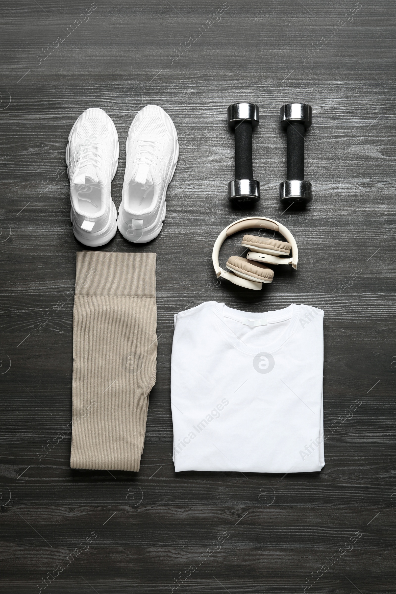 Photo of Stylish sportswear, white sneakers, dumbbells and headphones on wooden background, flat lay