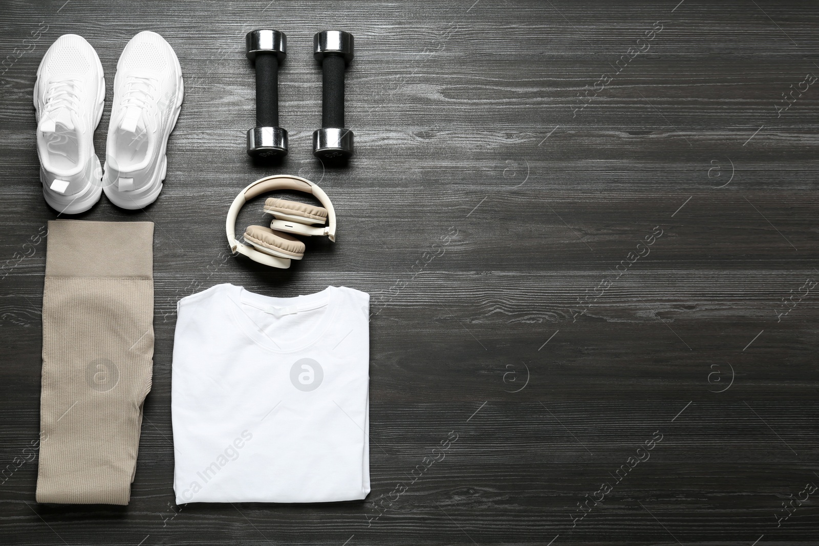 Photo of Stylish sportswear, white sneakers, dumbbells and headphones on wooden background, flat lay. Space for text