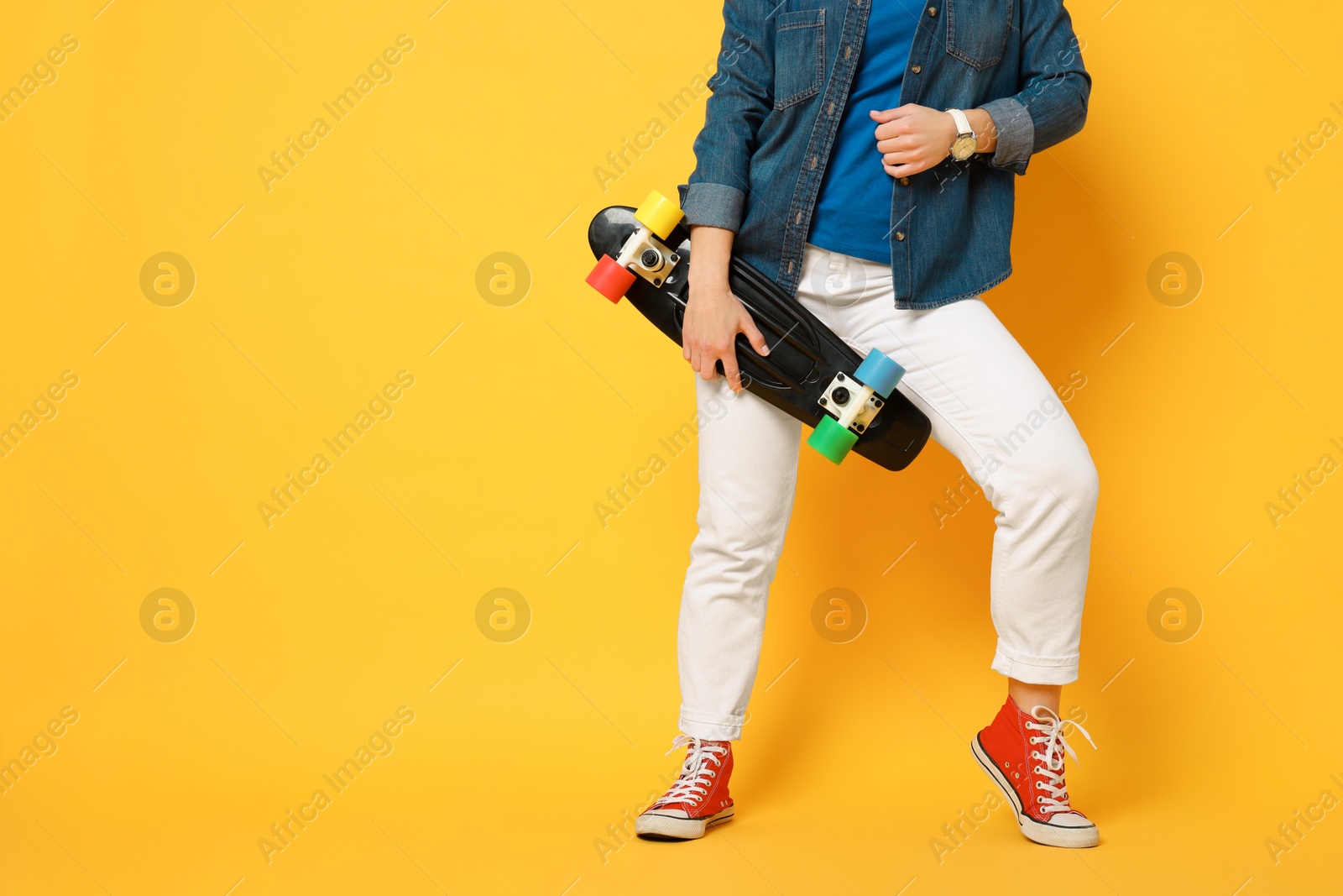 Photo of Woman with penny board on orange background, closeup. Space for text