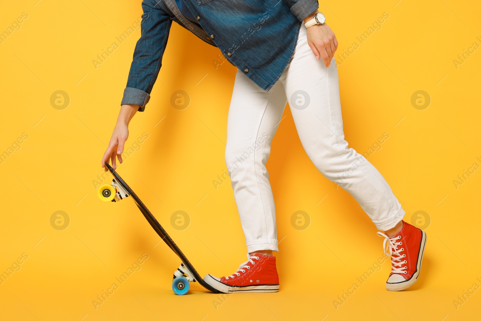 Photo of Woman with penny board on orange background, closeup