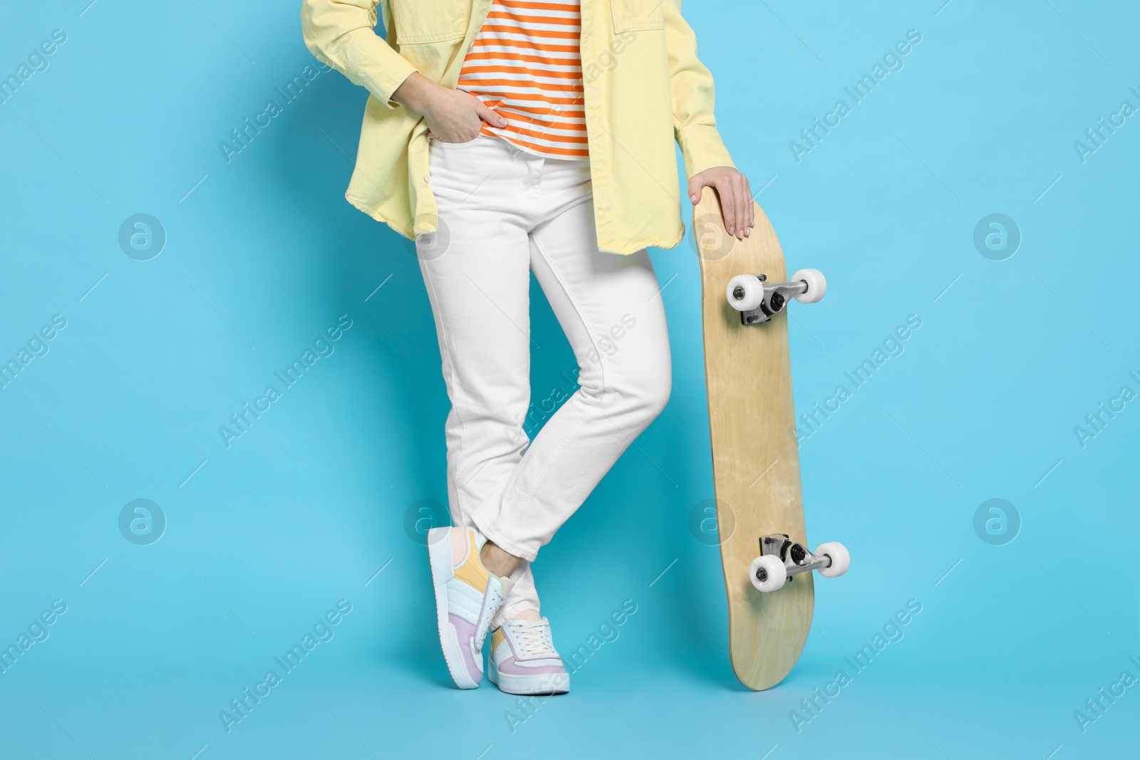 Photo of Woman with skateboard on light blue background, closeup