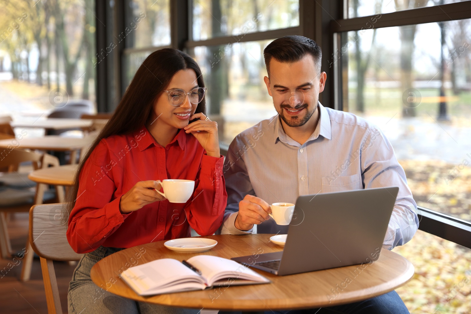 Photo of Colleagues with cups of coffee and laptop working together in cafe