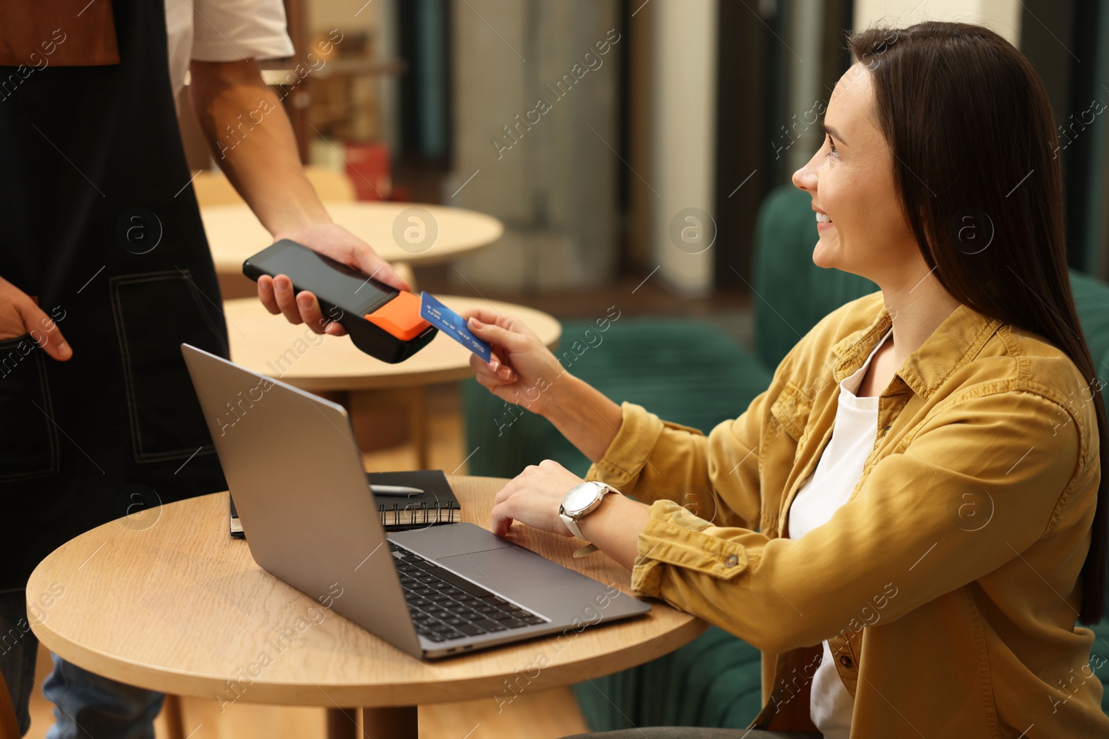 Photo of Woman paying with credit card via terminal at wooden table in cafe