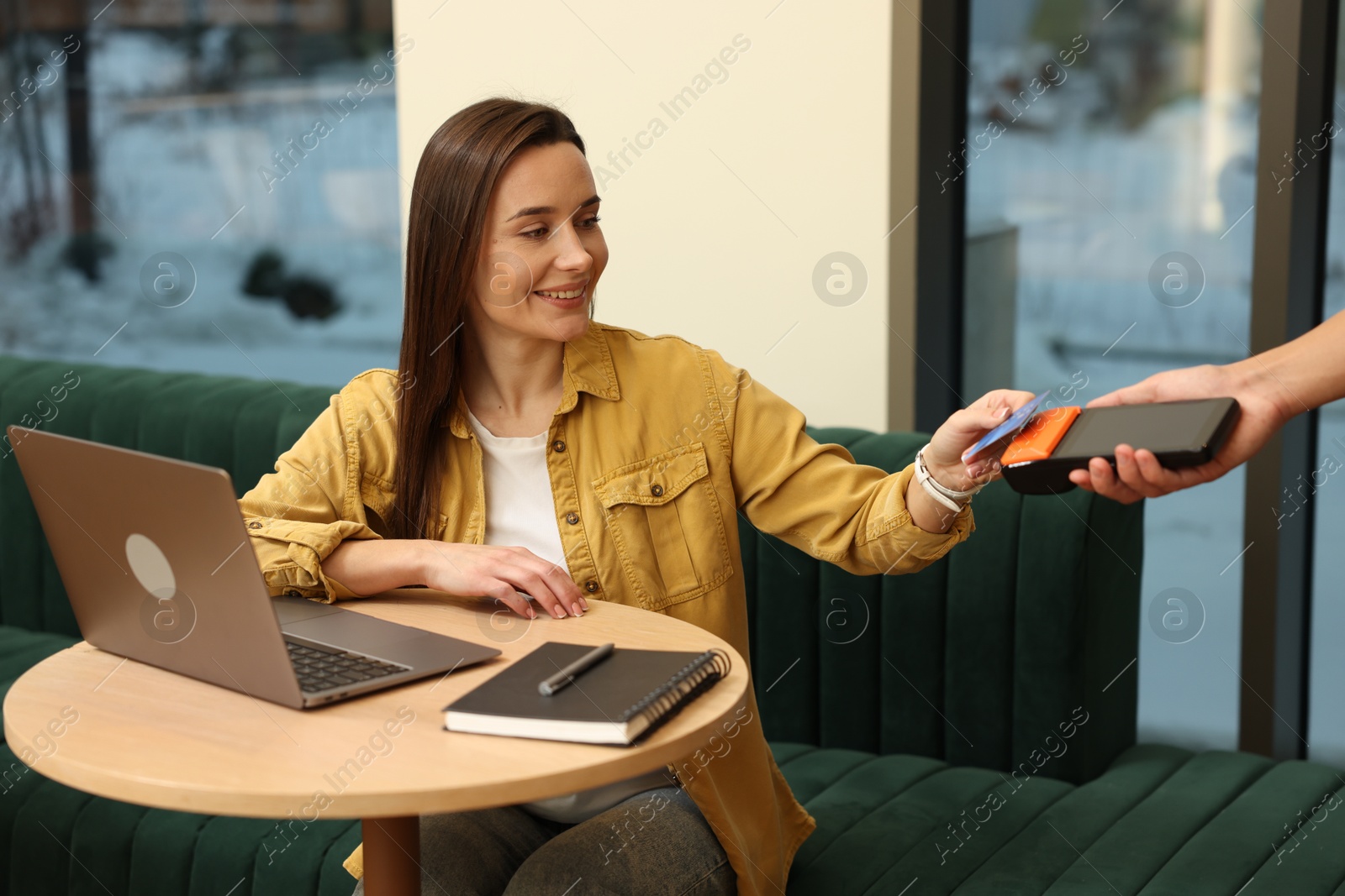 Photo of Woman paying with credit card via terminal at wooden table in cafe