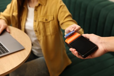 Photo of Woman paying with credit card via terminal in cafe, closeup