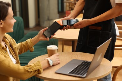 Photo of Woman paying with smartphone via terminal at wooden table in cafe