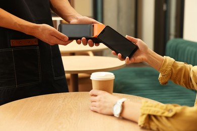 Photo of Woman paying with smartphone via terminal at wooden table in cafe, closeup