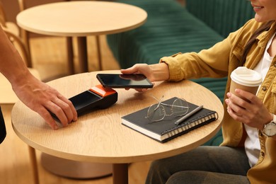 Photo of Woman paying with smartphone via terminal at wooden table in cafe, closeup