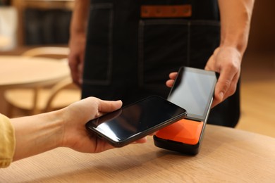 Photo of Woman paying with smartphone via terminal at wooden table in cafe, closeup