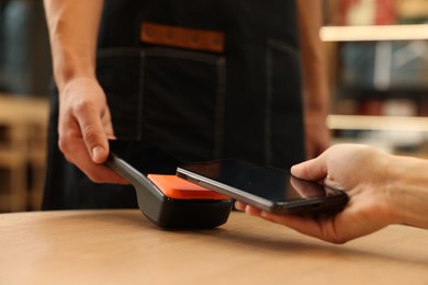 Photo of Woman paying with smartphone via terminal at wooden table in cafe, closeup