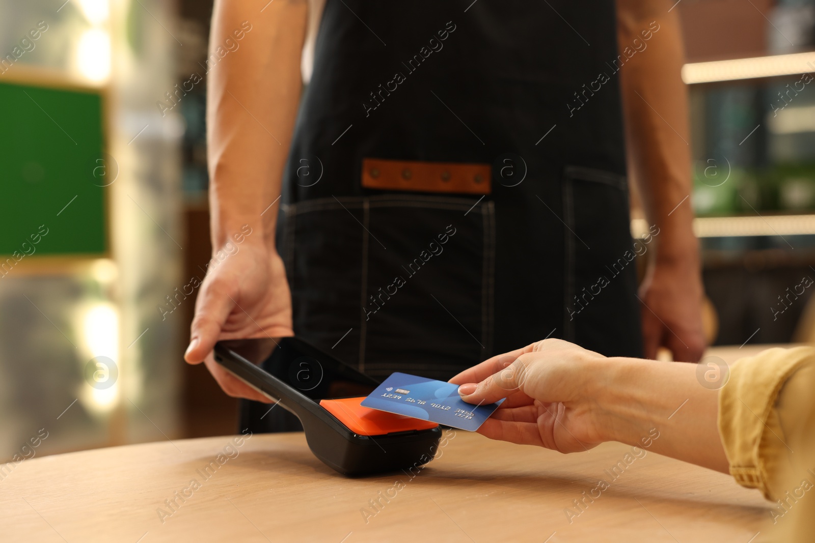 Photo of Woman paying with credit card via terminal at wooden table in cafe, closeup