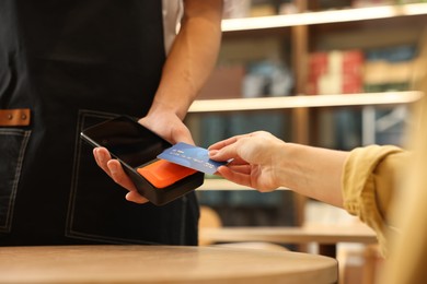 Photo of Woman paying with credit card via terminal at wooden table in cafe, closeup