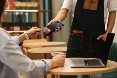 Photo of Woman paying with credit card via terminal at wooden table in cafe, closeup