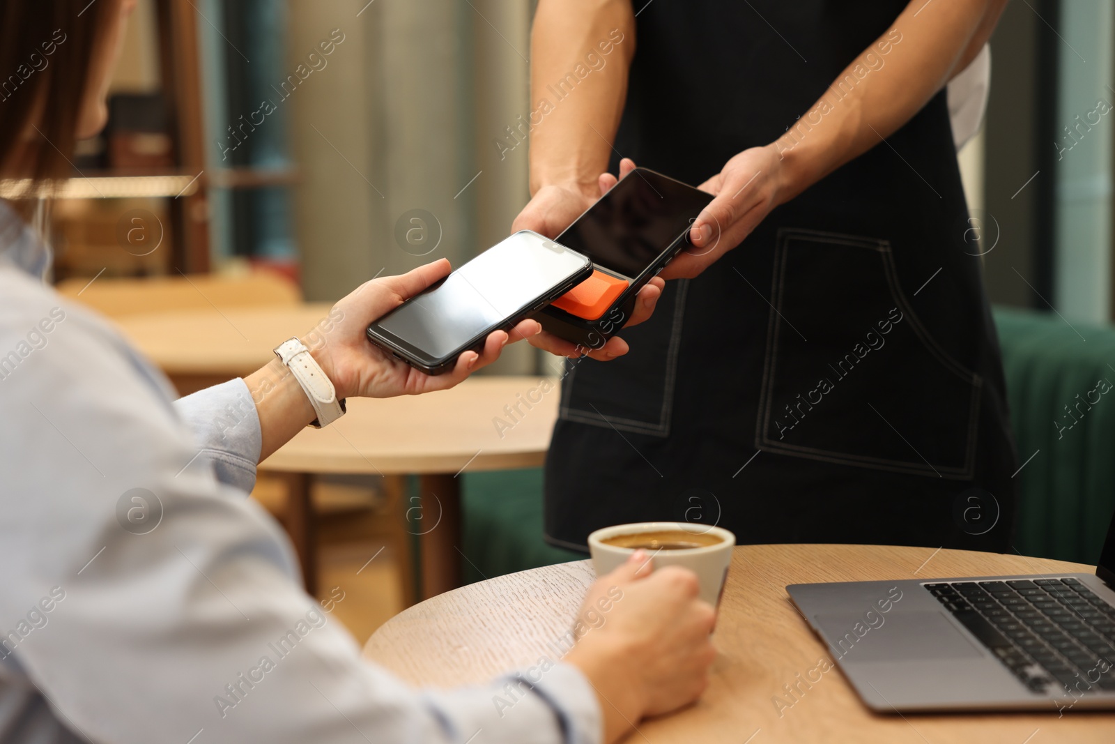 Photo of Woman paying with smartphone via terminal at wooden table in cafe, closeup