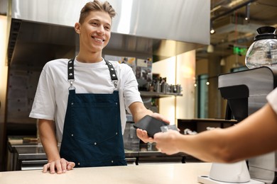 Photo of Cafe worker taking payment from client via terminal indoors