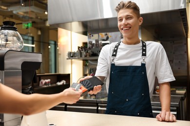 Photo of Cafe worker taking payment from client via terminal indoors