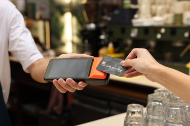 Photo of Woman paying with credit card via terminal in cafe, closeup