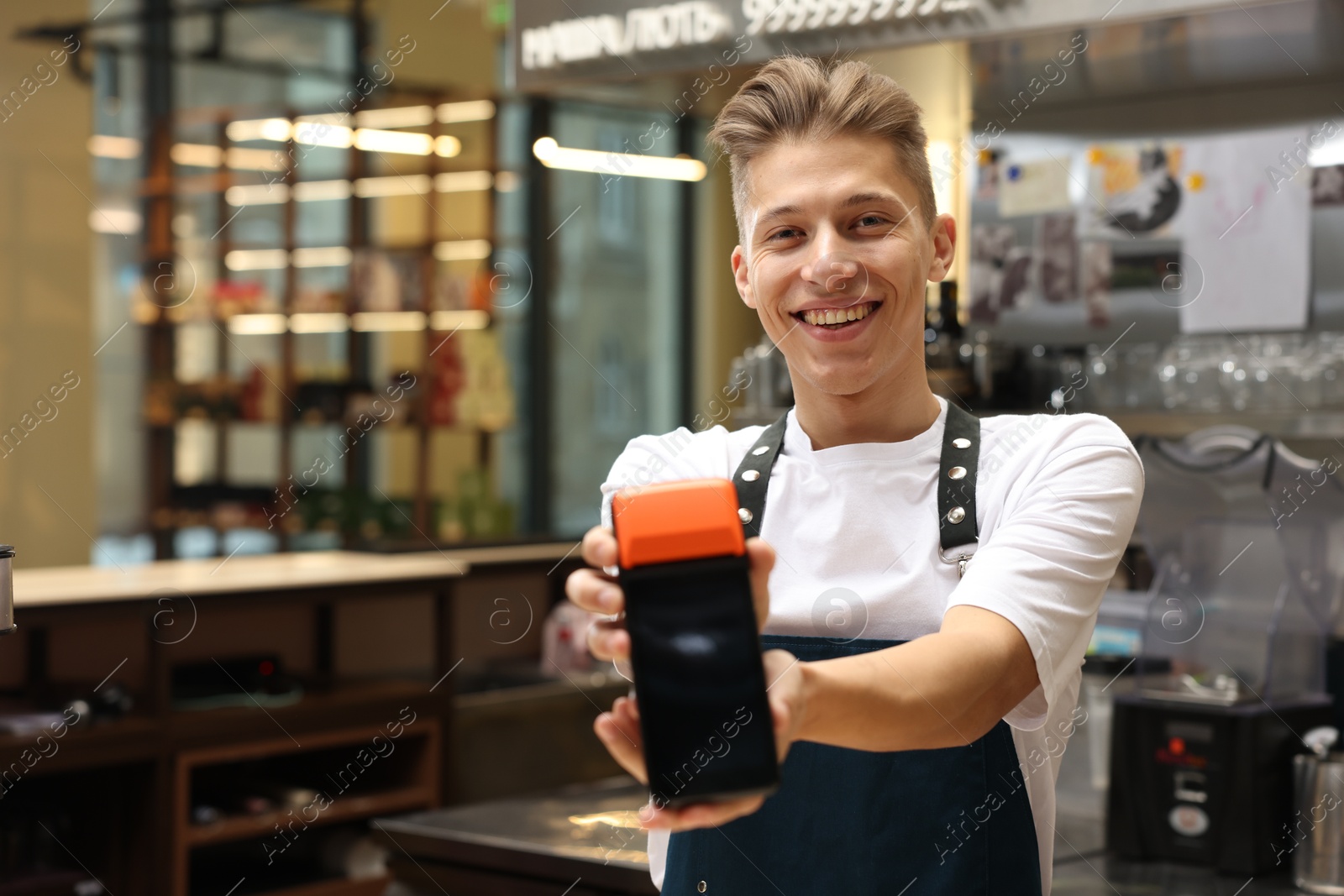 Photo of Smiling cafe worker with payment terminal indoors