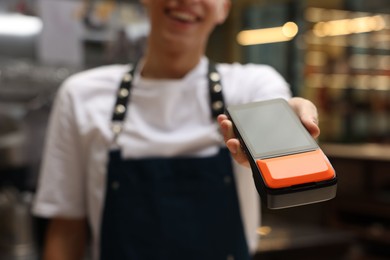 Photo of Cafe worker with payment terminal indoors, closeup