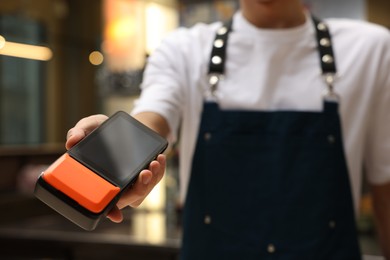 Photo of Cafe worker with payment terminal indoors, closeup