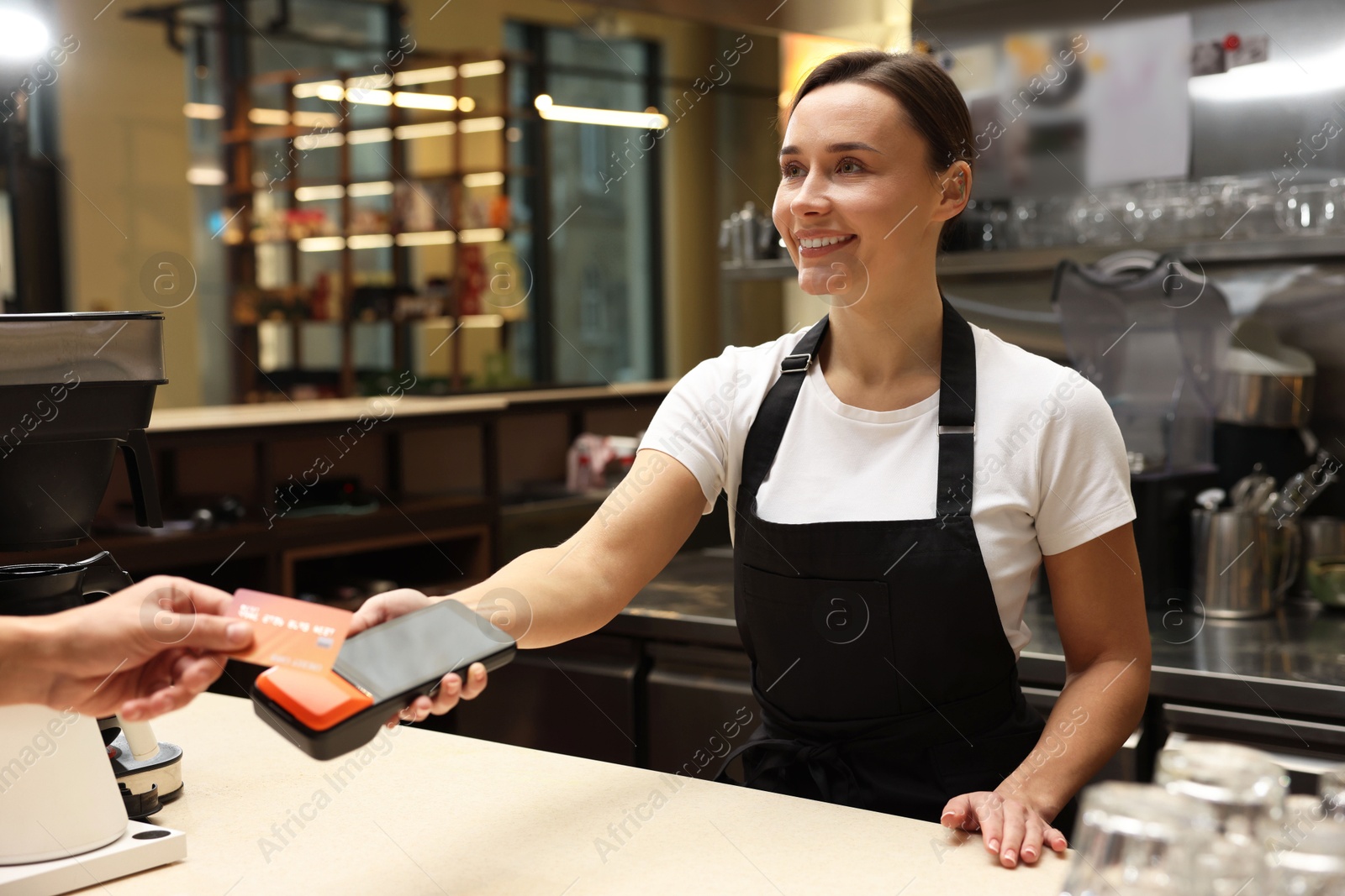 Photo of Cafe worker taking payment from client via terminal indoors