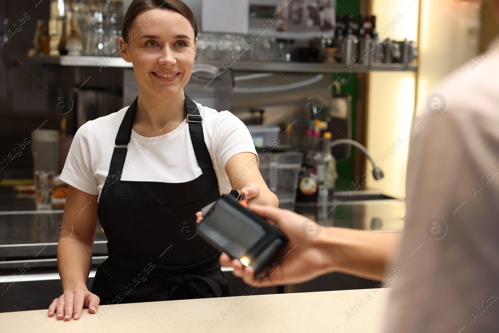 Photo of Cafe worker taking payment from client via terminal indoors