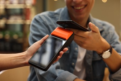 Photo of Man paying with smartphone via terminal in cafe, closeup