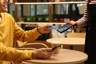 Photo of Man paying with credit card via terminal at wooden table in cafe, closeup