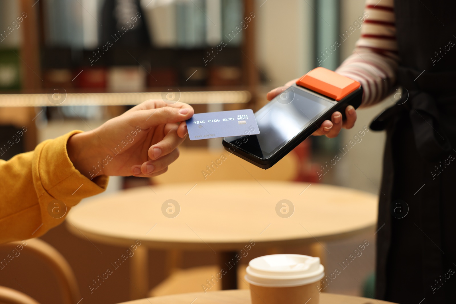 Photo of Man paying with credit card via terminal at wooden table in cafe, closeup