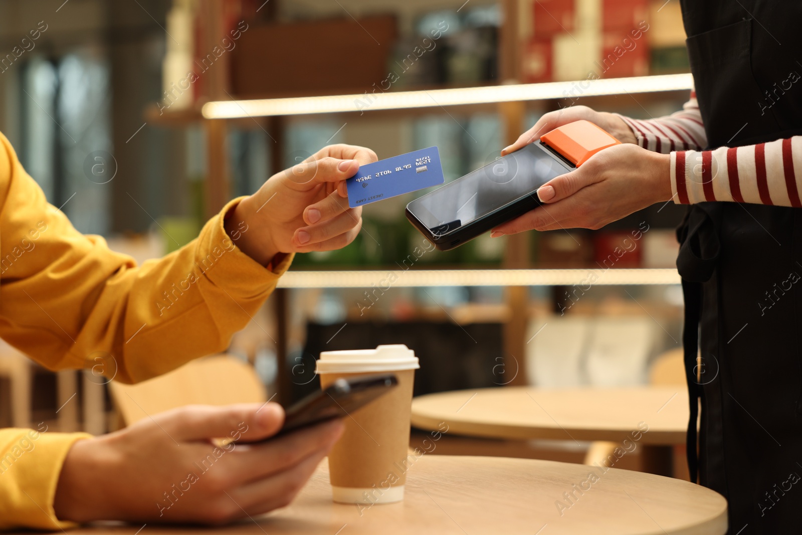 Photo of Man paying with credit card via terminal at wooden table in cafe, closeup