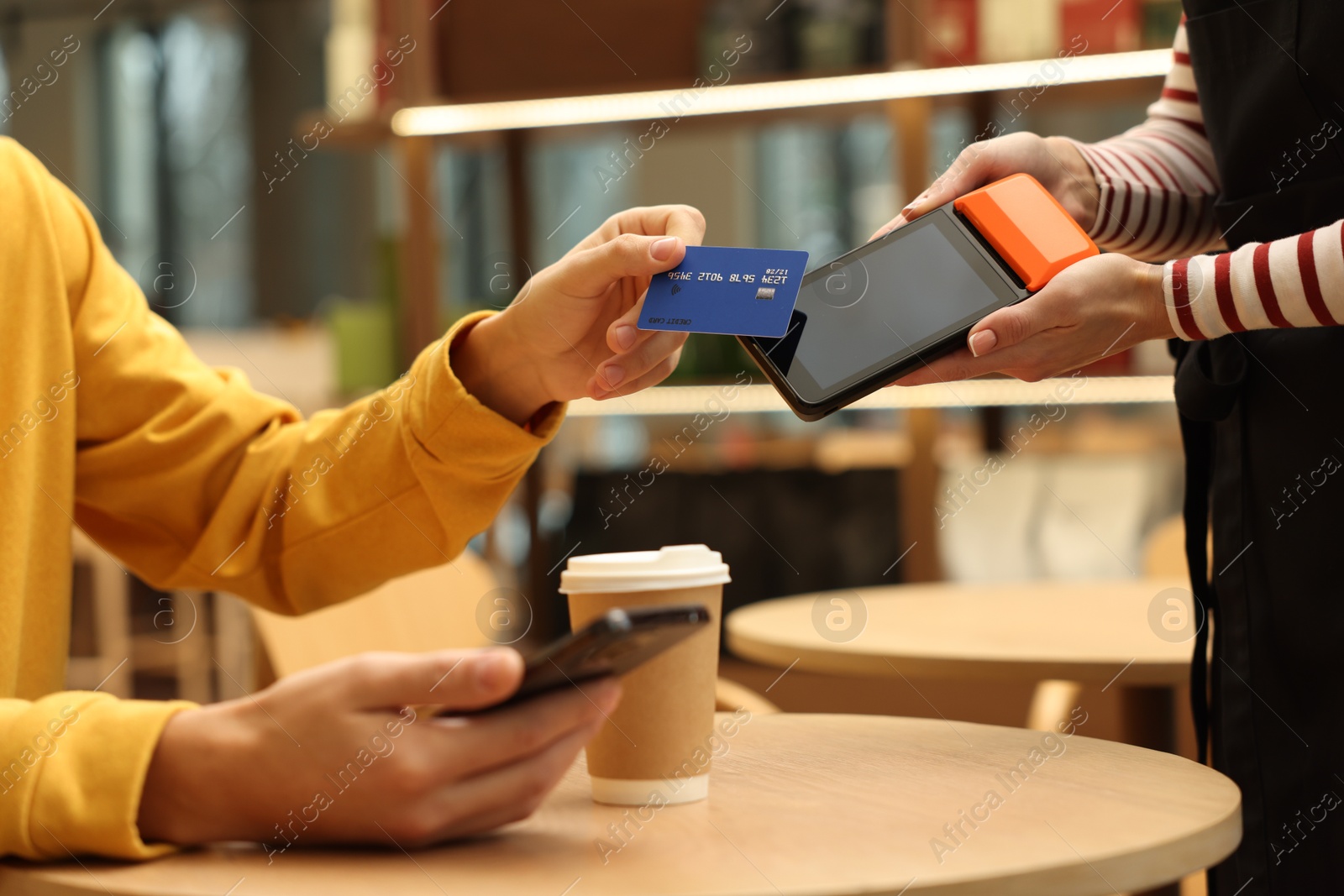 Photo of Man paying with credit card via terminal at wooden table in cafe, closeup