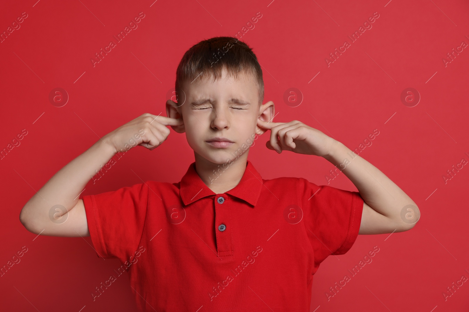 Photo of Little boy covering his ears with fingers on red background