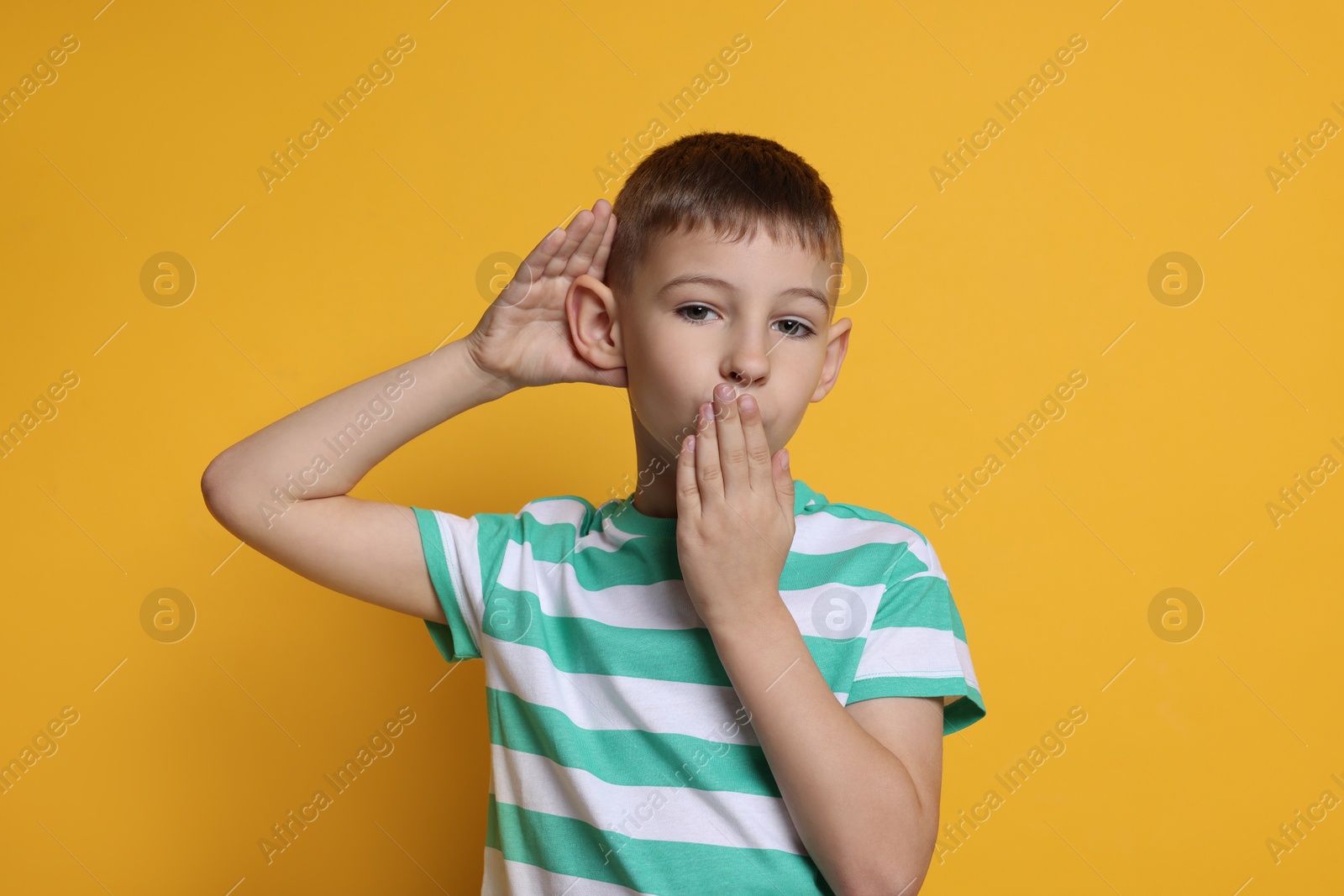 Photo of Little boy showing hand to ear gesture on orange background