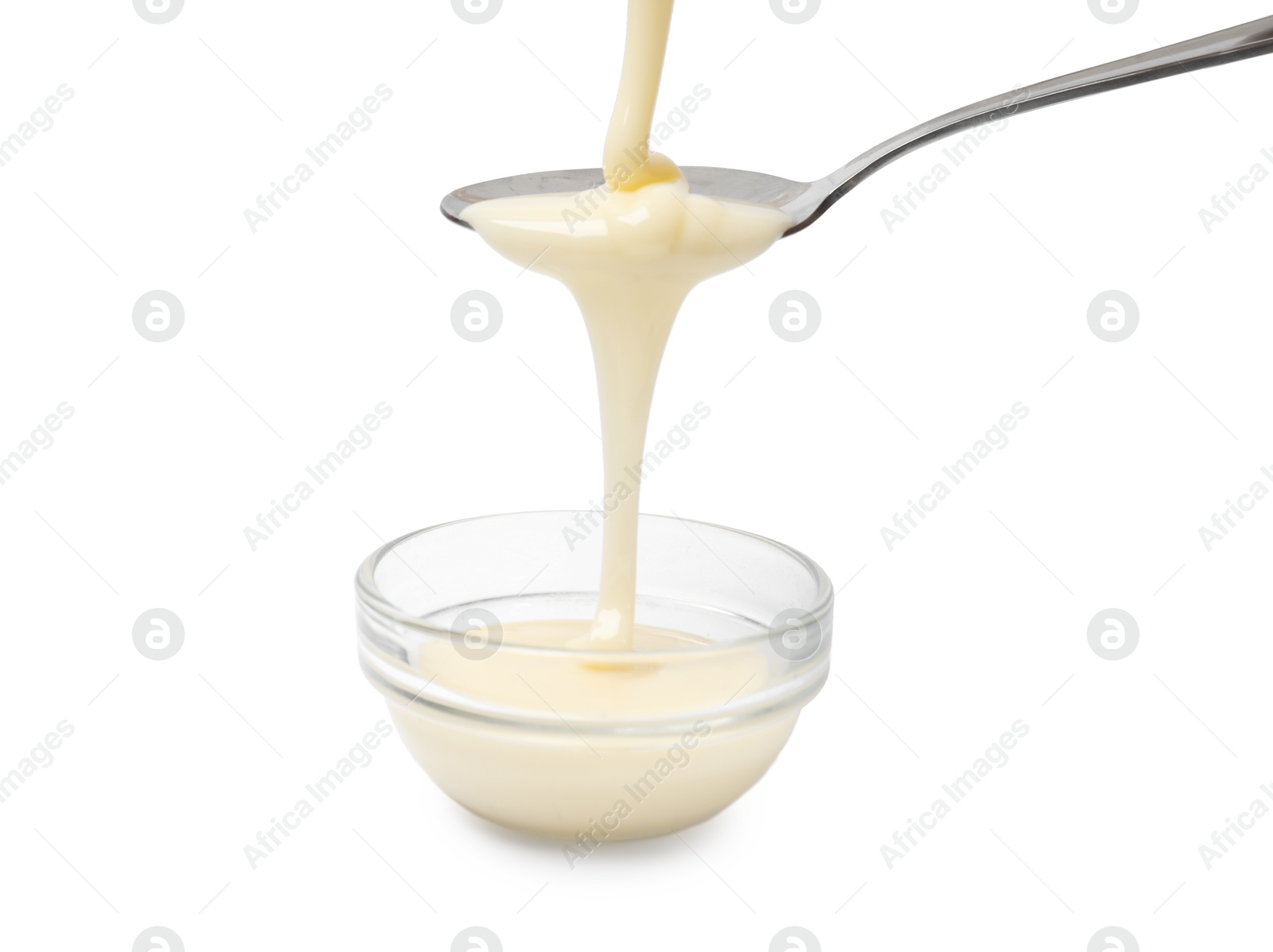 Photo of Condensed milk flowing down from spoon into bowl isolated on white