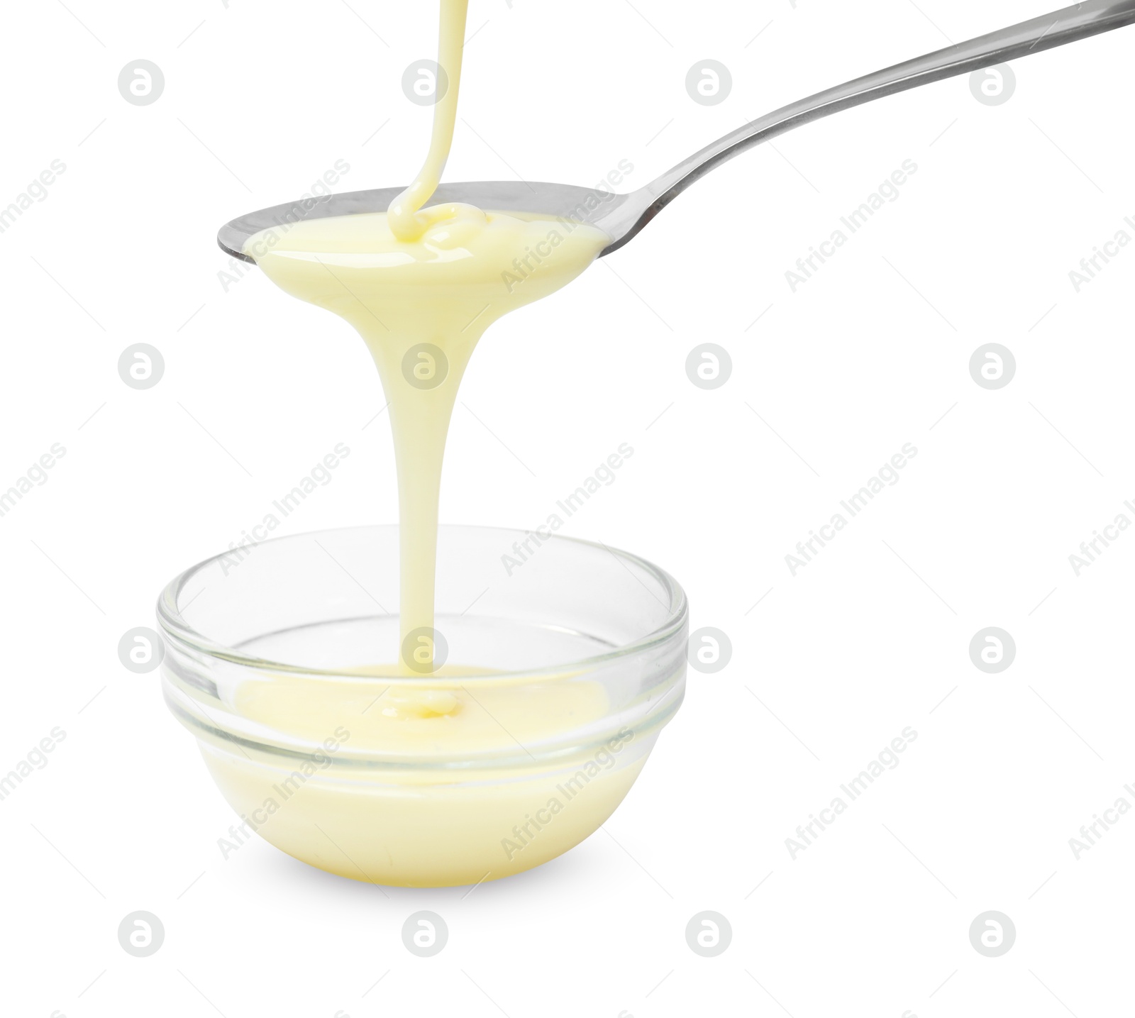 Photo of Condensed milk flowing down from spoon into bowl isolated on white