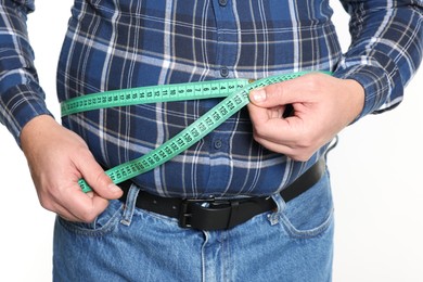 Photo of Overweight man measuring his belly with tape on white background, closeup