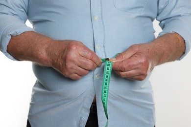 Photo of Overweight man measuring his belly with tape on white background, closeup