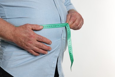 Photo of Overweight man measuring his belly with tape on white background, closeup. Space for text