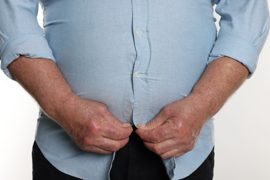 Photo of Overweight man trying to button up tight shirt on white background, closeup