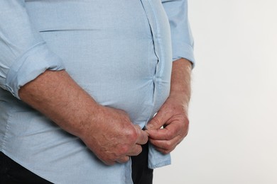 Photo of Overweight man trying to button up tight shirt on white background, closeup. Space for text