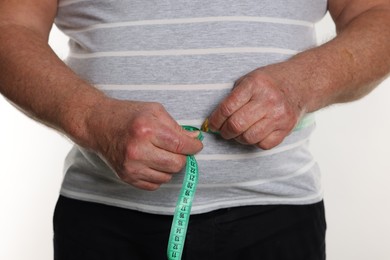 Photo of Overweight man measuring his belly with tape on white background, closeup