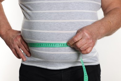 Photo of Overweight man measuring his belly with tape on white background, closeup