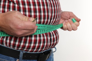 Photo of Overweight man measuring his belly with tape on white background, closeup