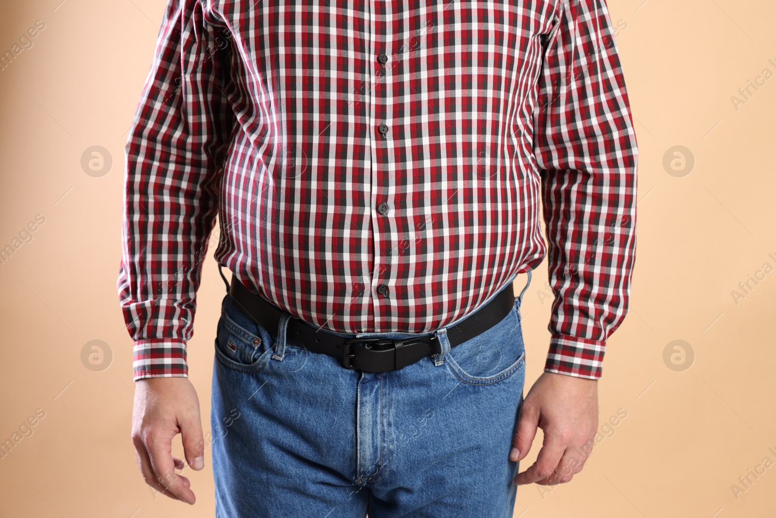 Photo of Overweight man in tight shirt on beige background, closeup