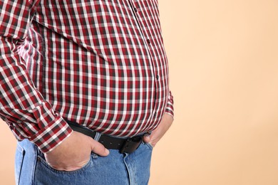 Photo of Overweight man in tight shirt on beige background, closeup. Space for text