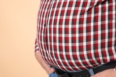 Photo of Overweight man in tight shirt on beige background, closeup. Space for text