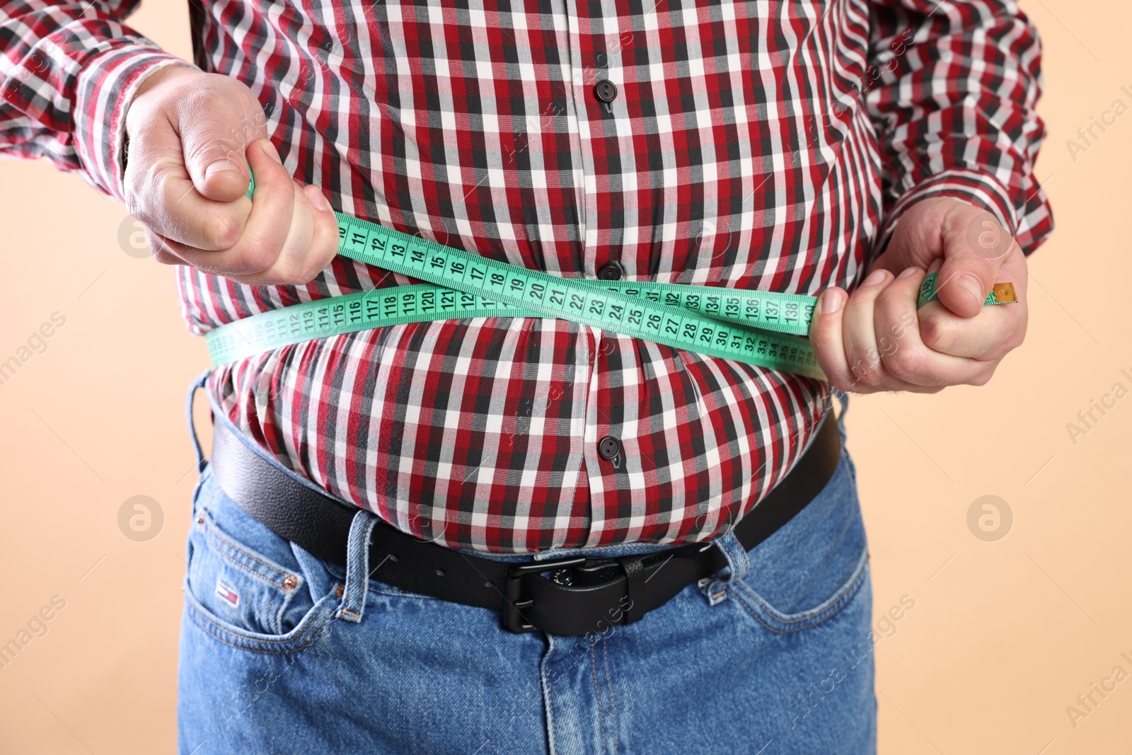 Photo of Overweight man measuring his belly with tape on beige background, closeup