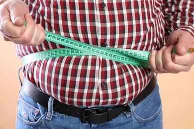 Photo of Overweight man measuring his belly with tape on beige background, closeup