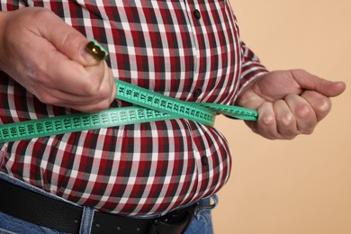 Photo of Overweight man measuring his belly with tape on beige background, closeup