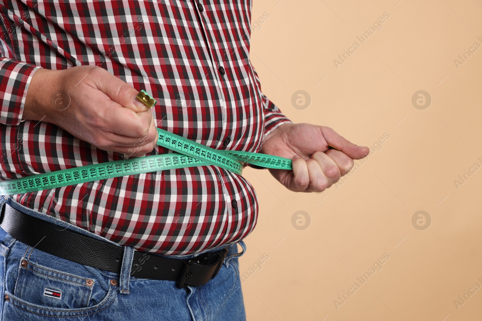 Photo of Overweight man measuring his belly with tape on beige background, closeup. Space for text